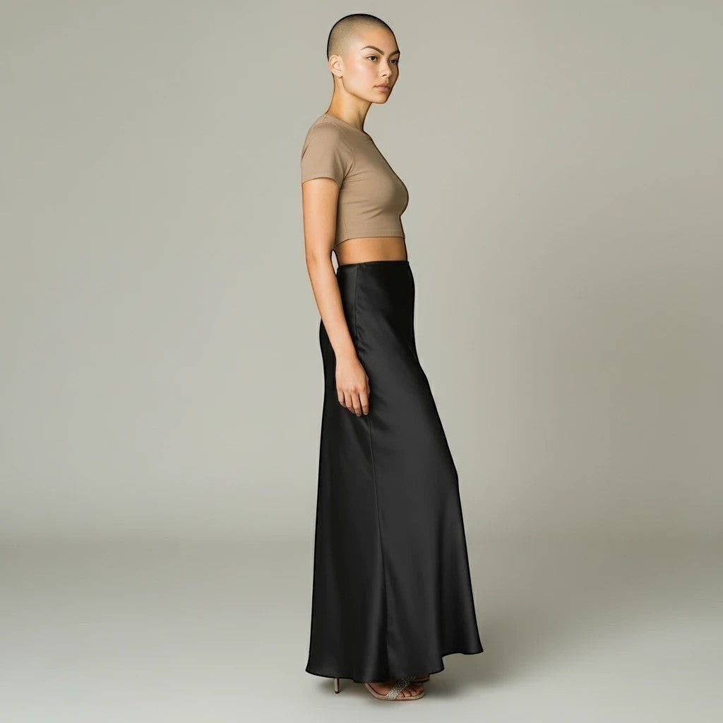 Model wearing a Lavishly Me black satin maxi skirt with a beige cropped t-shirt in a side profile view.