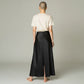 Model wearing a Lavishly Me black satin maxi skirt with a back slit, paired with a beige t-shirt, back view.