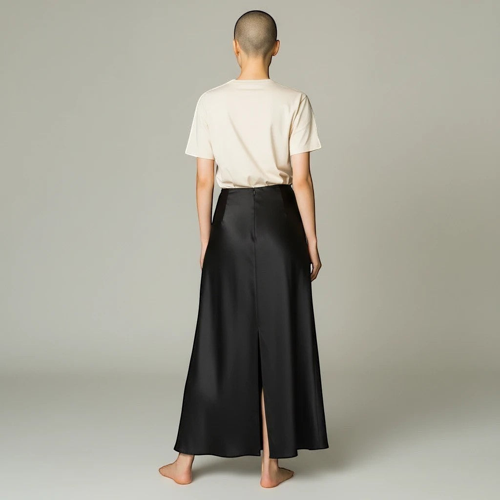 Model wearing a Lavishly Me black satin maxi skirt with a back slit, paired with a beige t-shirt, back view.