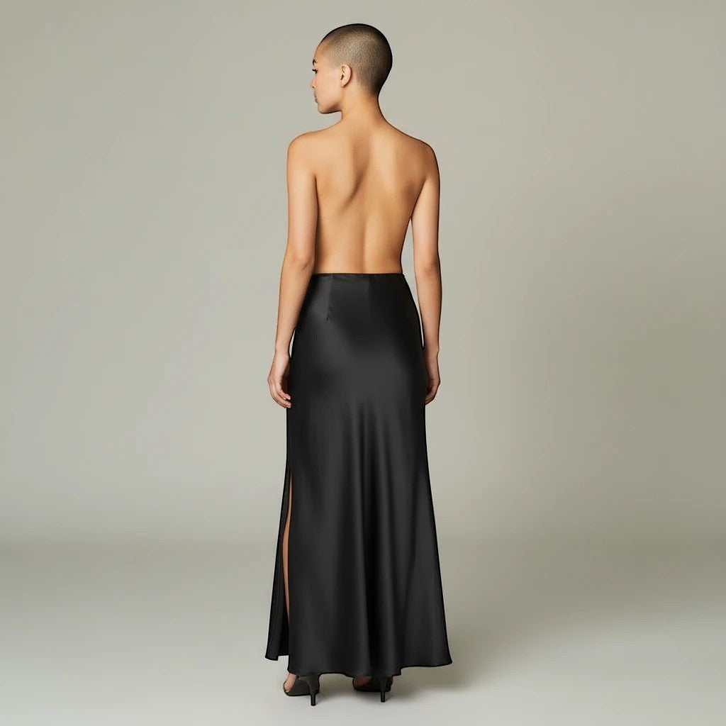 Model wearing a Lavishly Me black satin maxi skirt with a side slit, viewed from the back.