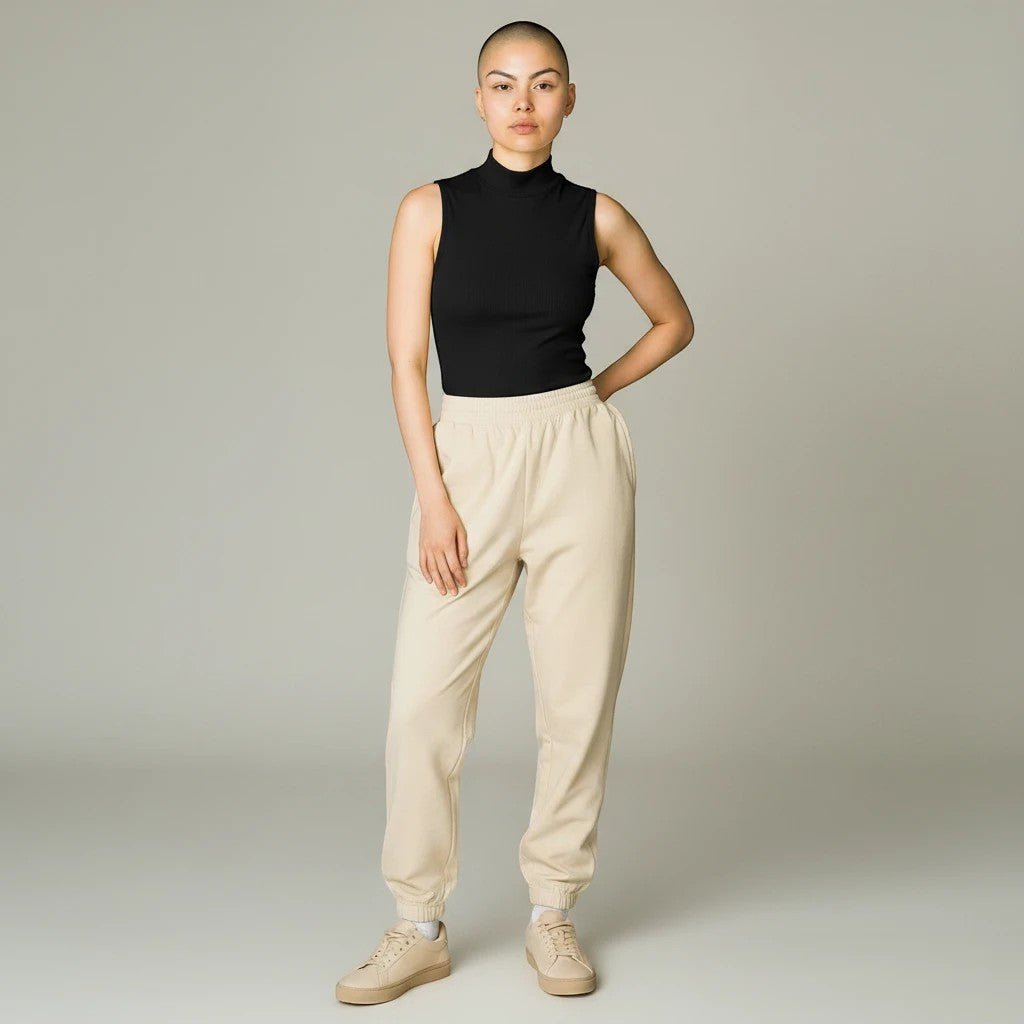 Model wearing a black Lavishly Me sleeveless turtleneck top with beige joggers and sneakers in a studio setting.