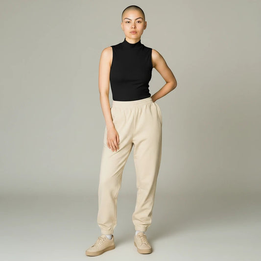 Model wearing a black Lavishly Me sleeveless turtleneck top with beige joggers and sneakers in a studio setting.