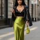 A model wearing a Lavishly Me lime green satin fishtail skirt with a black crop top and leather jacket on a city street.