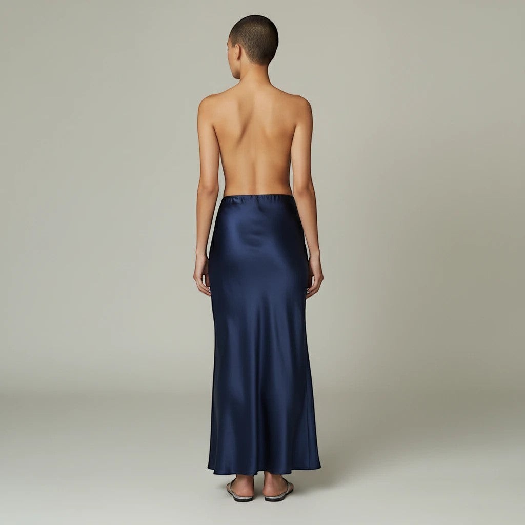 Model wearing a Lavishly Me navy blue satin maxi skirt with a fluid, floor-length silhouette, back view.