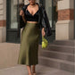 Woman wearing a Lavishly Me olive green satin fishtail skirt with a black crop top and leather jacket on city steps.