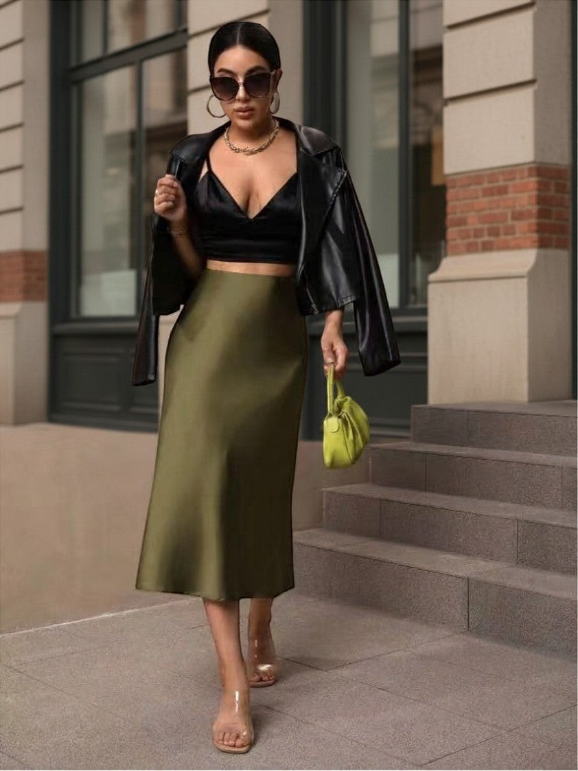 Woman wearing a Lavishly Me olive green satin fishtail skirt with a black crop top and leather jacket on city steps.