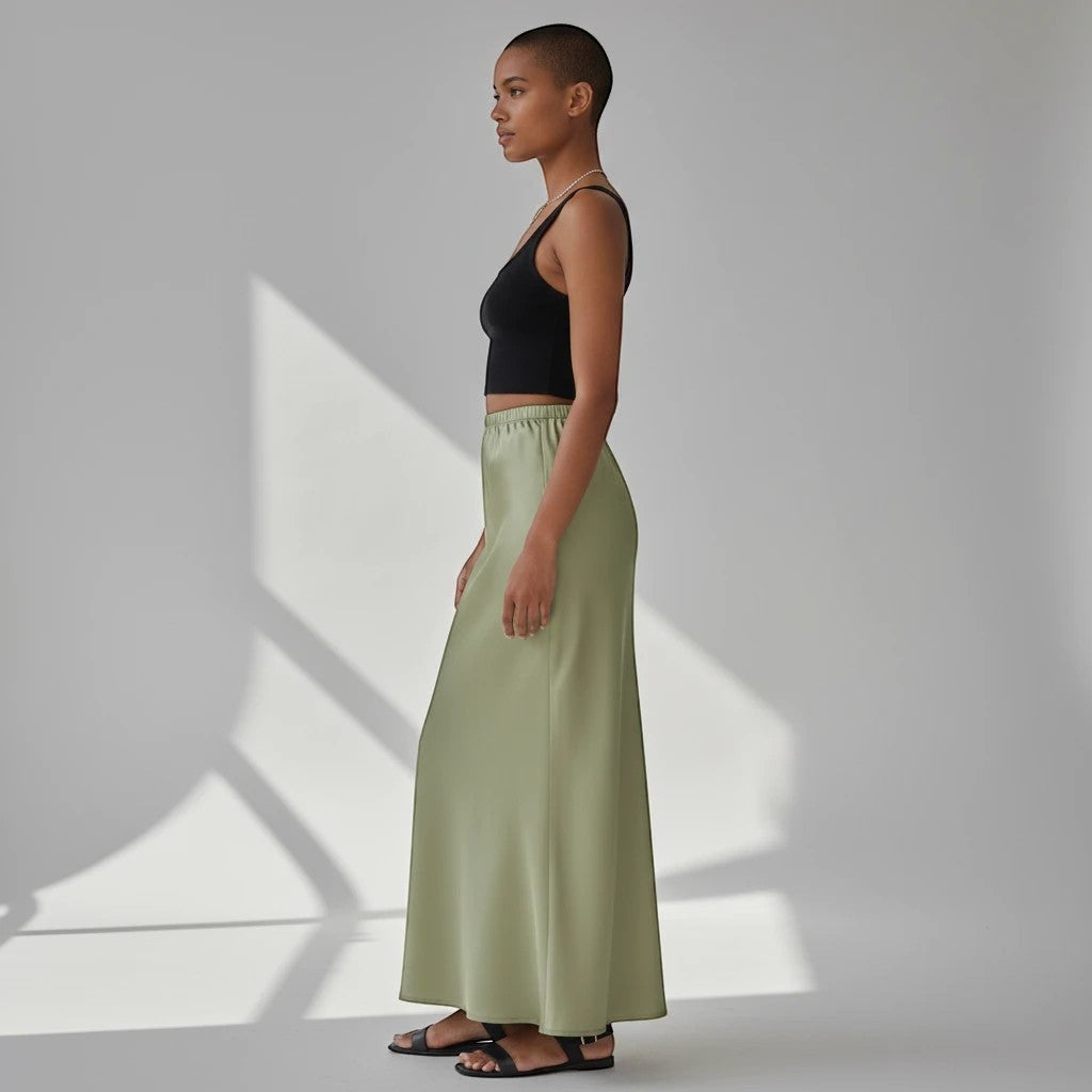 Model wearing a Lavishly Me sage green satin maxi skirt with a black tank top in a minimalist studio setting