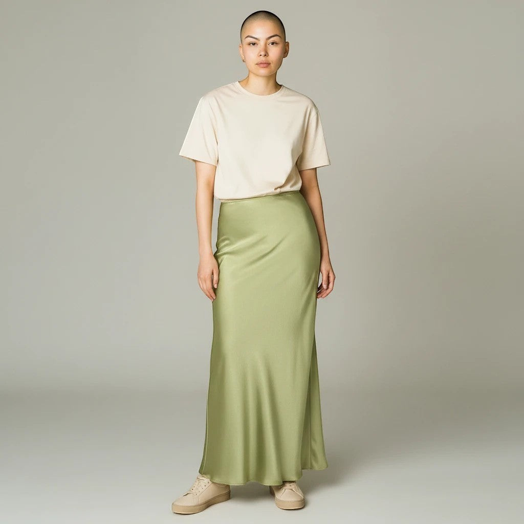 Model wearing a Lavishly Me sage green satin maxi skirt with a beige t-shirt and sneakers in a studio setting